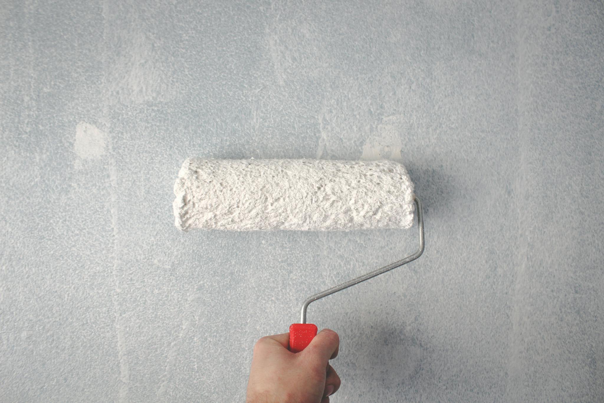 A person's hand using a paint roller to apply white paint on a wall Denver painting company